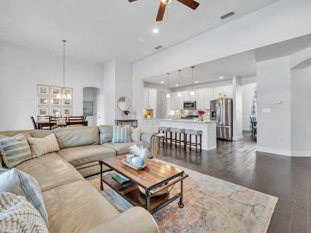 living area with ceiling fan with notable chandelier, arched walkways, visible vents, recessed lighting, and dark wood-style flooring