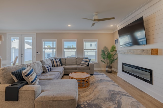 living area with crown molding, french doors, wood finished floors, a glass covered fireplace, and a ceiling fan