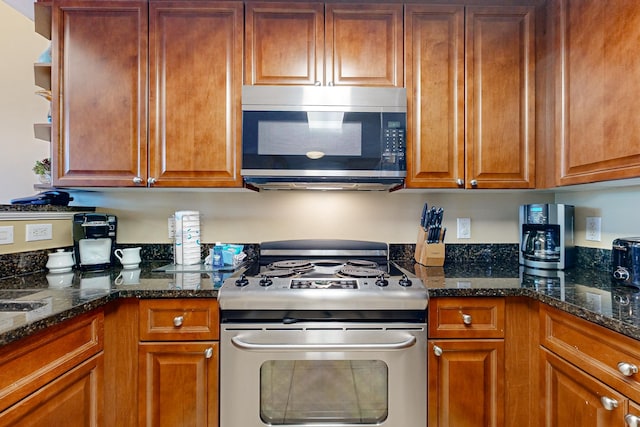 kitchen featuring dark stone countertops, stainless steel appliances, and brown cabinetry