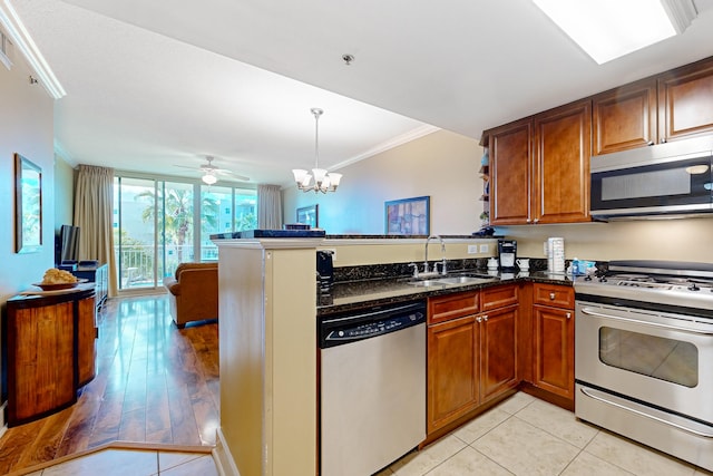 kitchen featuring ornamental molding, a sink, dark stone counters, appliances with stainless steel finishes, and a peninsula