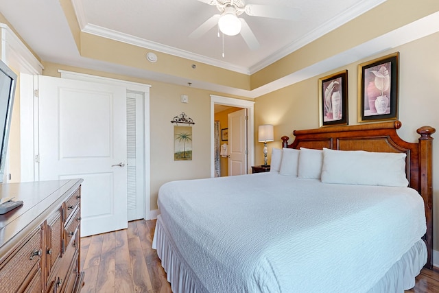 bedroom with dark wood finished floors, a ceiling fan, a tray ceiling, and ornamental molding