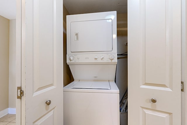 clothes washing area featuring light tile patterned floors, stacked washer / dryer, and laundry area