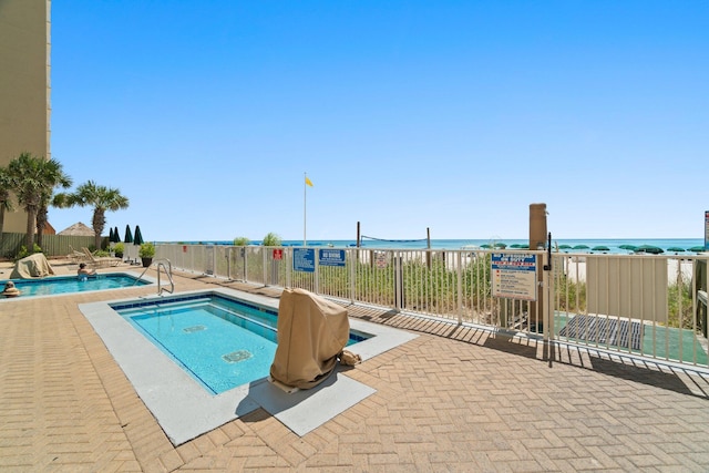 community pool with a water view, fence, and a hot tub