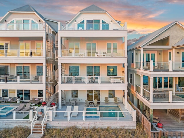 back of property at dusk with a pool with connected hot tub and a patio area