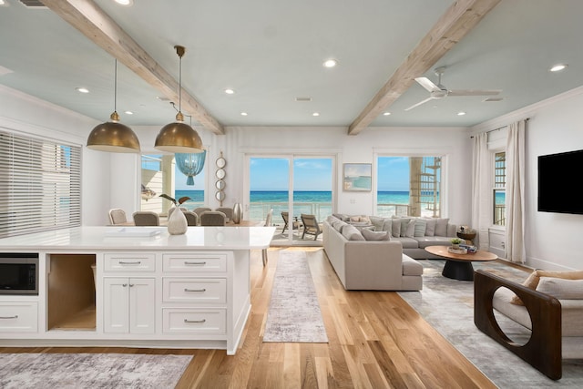 kitchen featuring beamed ceiling, light wood-style flooring, stainless steel microwave, open floor plan, and white cabinets