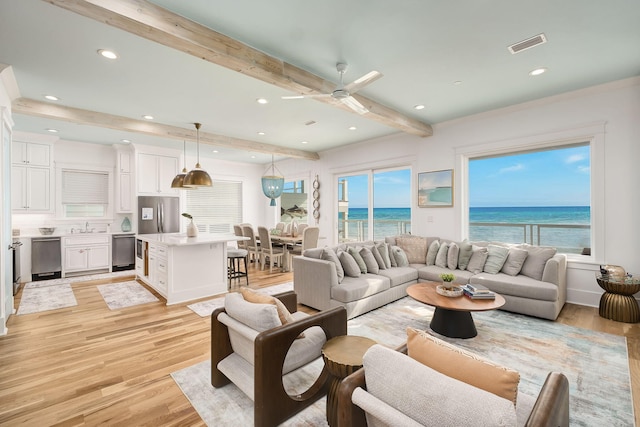 living area with beam ceiling, visible vents, a healthy amount of sunlight, and light wood-style flooring