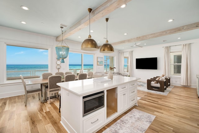 kitchen with light wood finished floors, white cabinetry, stainless steel microwave, beamed ceiling, and a center island