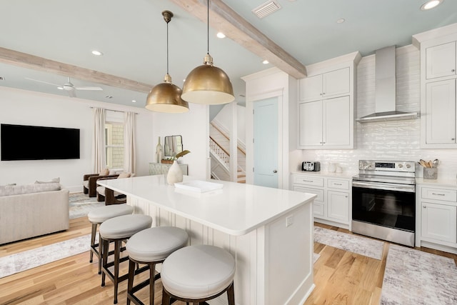 kitchen with light wood finished floors, visible vents, wall chimney range hood, beam ceiling, and stainless steel electric range