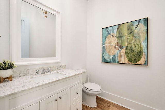 bathroom with toilet, vanity, baseboards, and wood finished floors