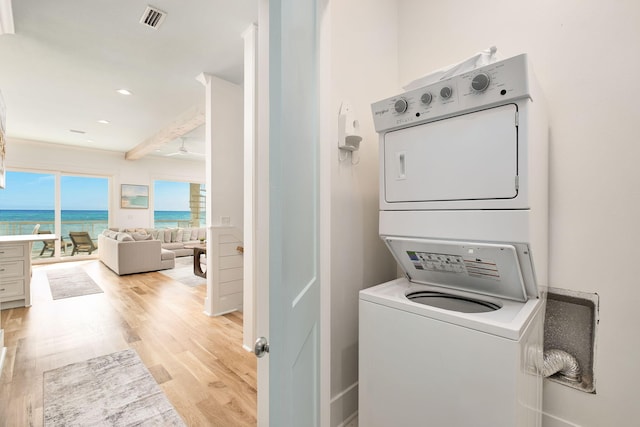 washroom featuring visible vents, a water view, light wood-style flooring, stacked washing maching and dryer, and laundry area