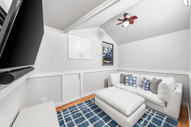 sitting room featuring a ceiling fan, lofted ceiling with beams, a wainscoted wall, a decorative wall, and wood finished floors