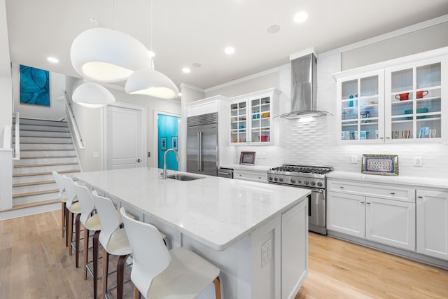 kitchen featuring wall chimney exhaust hood, high end appliances, a center island with sink, a sink, and backsplash