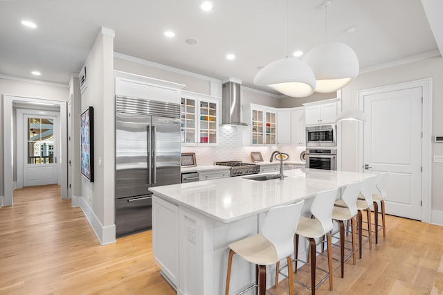 kitchen with wall chimney range hood, built in appliances, ornamental molding, and a sink