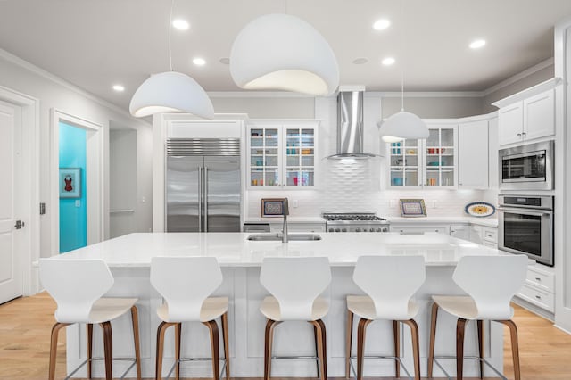 kitchen featuring wall chimney range hood, a sink, ornamental molding, and built in appliances