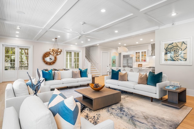 living area with beamed ceiling, stairway, a ceiling fan, light wood-type flooring, and coffered ceiling