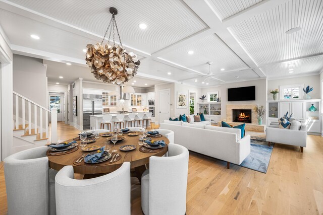 dining space featuring a lit fireplace, light wood-style flooring, recessed lighting, and beam ceiling