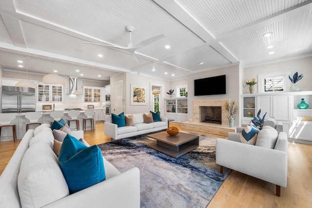 living area with coffered ceiling, a ceiling fan, light wood finished floors, a high end fireplace, and beamed ceiling
