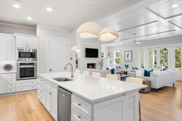 kitchen with a sink, a warm lit fireplace, appliances with stainless steel finishes, a center island with sink, and plenty of natural light