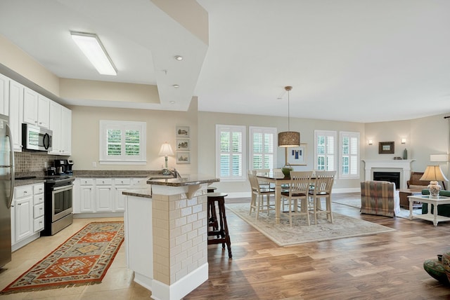 kitchen with light wood-style flooring, dark stone countertops, a kitchen breakfast bar, appliances with stainless steel finishes, and a raised ceiling