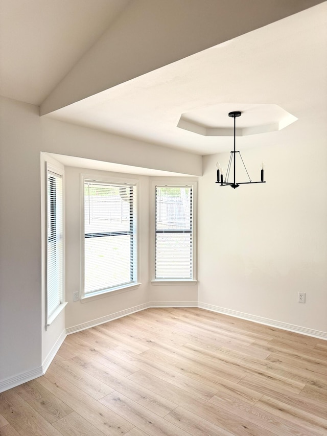 unfurnished room featuring baseboards, a notable chandelier, a raised ceiling, and light wood-style floors