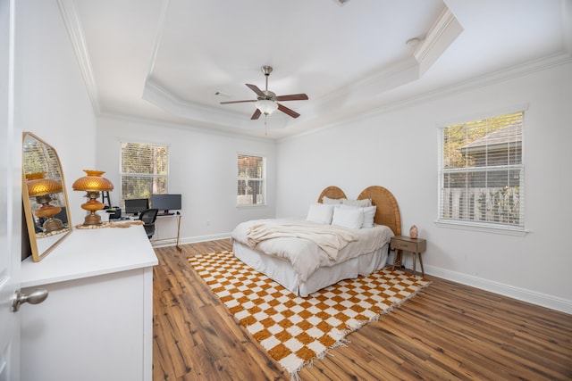 bedroom with a tray ceiling, wood finished floors, and ornamental molding