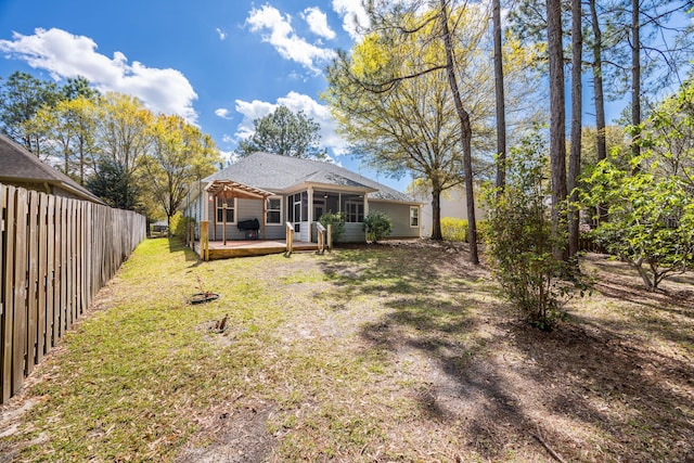 rear view of house with a sunroom, roof with shingles, a wooden deck, fence, and a lawn