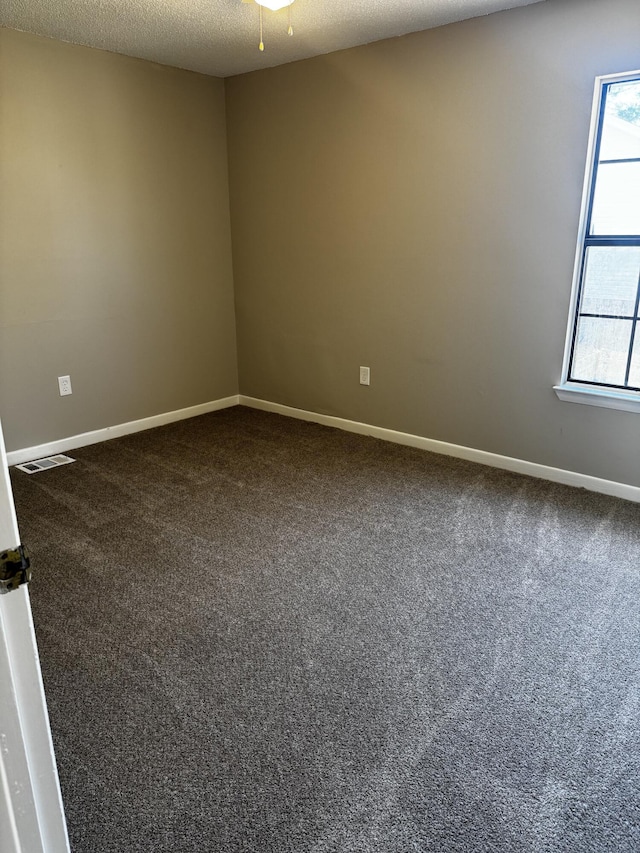 empty room with baseboards, visible vents, dark carpet, and a textured ceiling