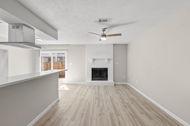 unfurnished living room featuring a ceiling fan, visible vents, baseboards, a textured ceiling, and light wood-type flooring