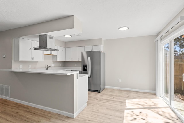 kitchen with visible vents, wall chimney range hood, stainless steel fridge with ice dispenser, light countertops, and a peninsula