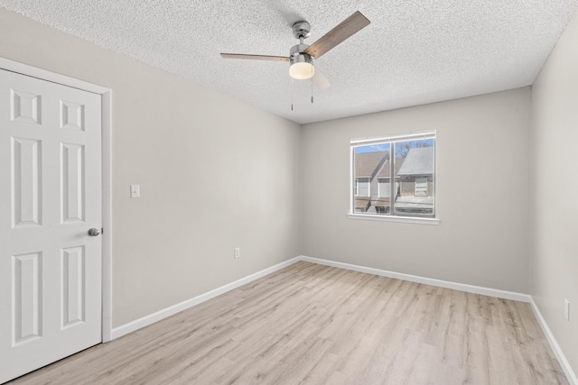 empty room with a textured ceiling, baseboards, light wood finished floors, and ceiling fan