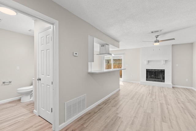 unfurnished living room featuring visible vents, baseboards, light wood-type flooring, a textured ceiling, and a ceiling fan