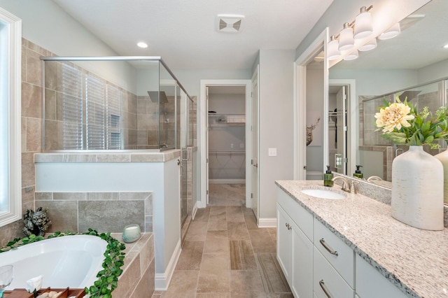 bathroom with vanity, baseboards, a shower stall, a walk in closet, and a garden tub