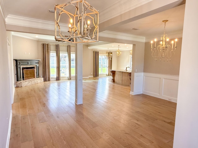 unfurnished dining area featuring a fireplace, light wood-style floors, wainscoting, and a chandelier