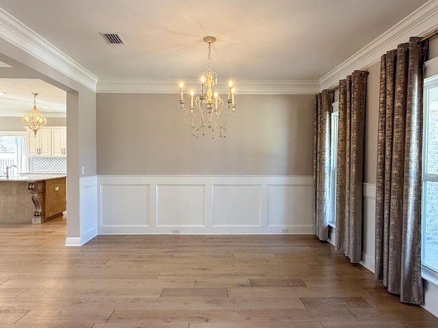 unfurnished dining area featuring a notable chandelier, visible vents, light wood finished floors, and ornamental molding