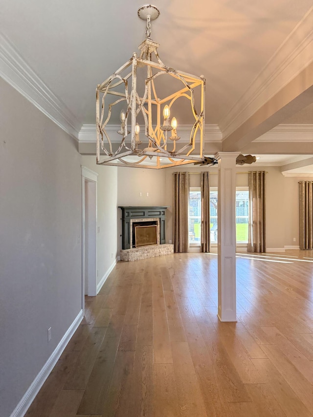 unfurnished living room featuring hardwood / wood-style floors, baseboards, a fireplace, ornamental molding, and a notable chandelier