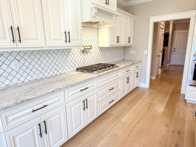 kitchen with light wood-style flooring, light stone counters, white cabinetry, stainless steel appliances, and decorative backsplash