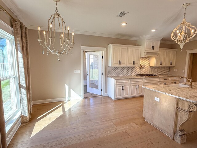 kitchen featuring visible vents, a sink, light wood-style floors, an inviting chandelier, and crown molding