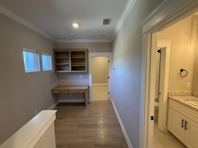 corridor with light wood-style flooring, baseboards, visible vents, and ornamental molding