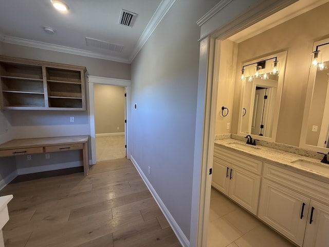 hall with a sink, visible vents, ornamental molding, and light wood-style flooring