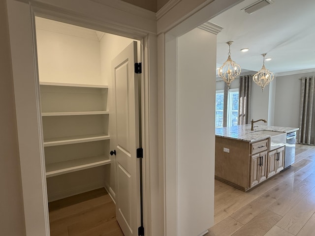 hallway with visible vents, crown molding, a chandelier, light wood-style flooring, and a sink