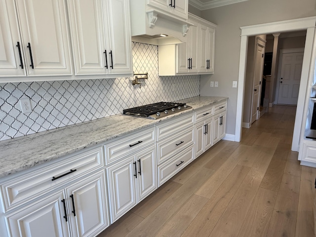 kitchen featuring light wood finished floors, tasteful backsplash, light stone countertops, appliances with stainless steel finishes, and white cabinetry