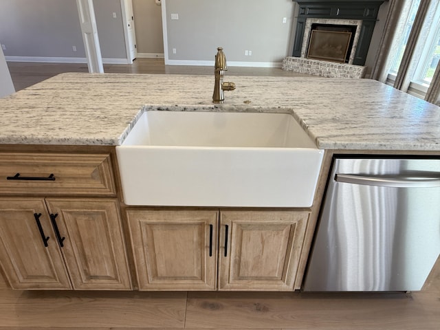 kitchen with dishwasher, light stone countertops, baseboards, and a sink