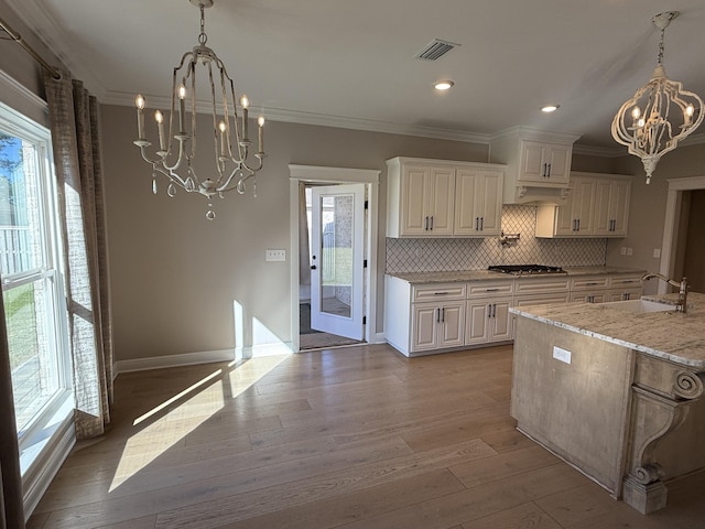 kitchen featuring visible vents, light wood-style flooring, ornamental molding, a sink, and a notable chandelier