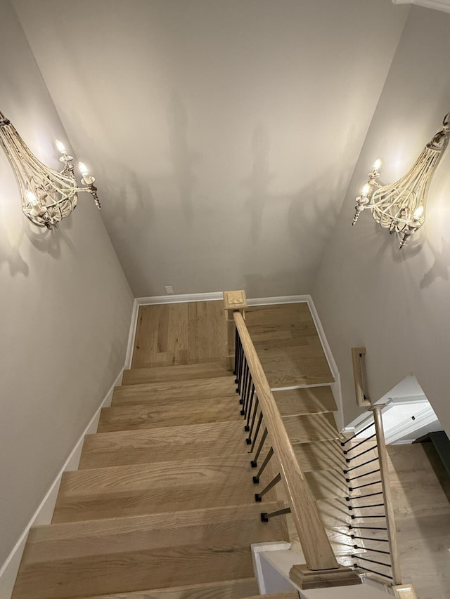 stairway featuring baseboards, an inviting chandelier, and wood finished floors