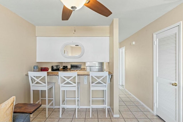 kitchen featuring a kitchen breakfast bar, refrigerator, a toaster, light tile patterned floors, and ceiling fan