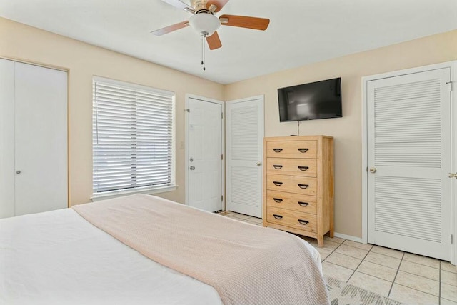 bedroom with light tile patterned floors, multiple closets, and ceiling fan