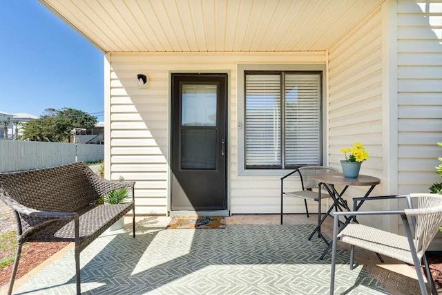 view of exterior entry with a patio area, a porch, and fence