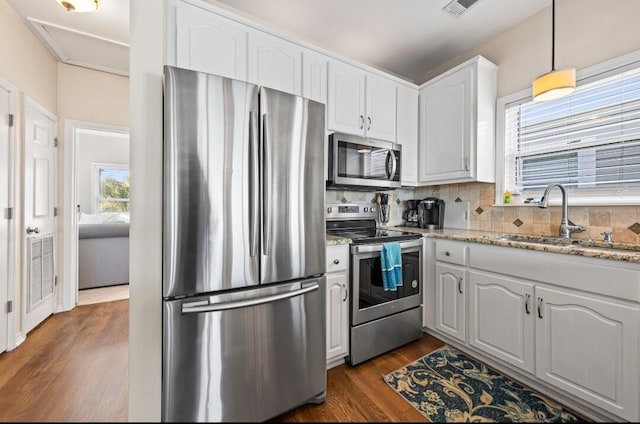 kitchen with light stone countertops, appliances with stainless steel finishes, white cabinets, a sink, and dark wood-type flooring