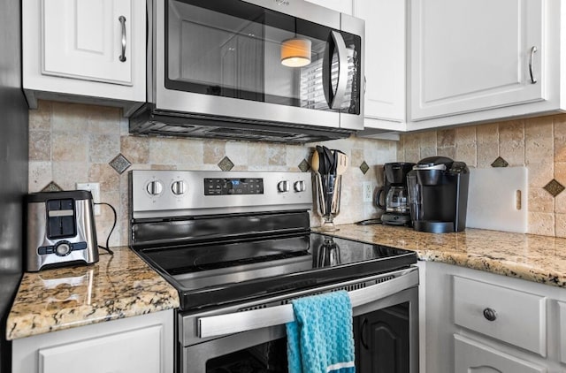 kitchen featuring white cabinets, stainless steel appliances, light stone countertops, and decorative backsplash