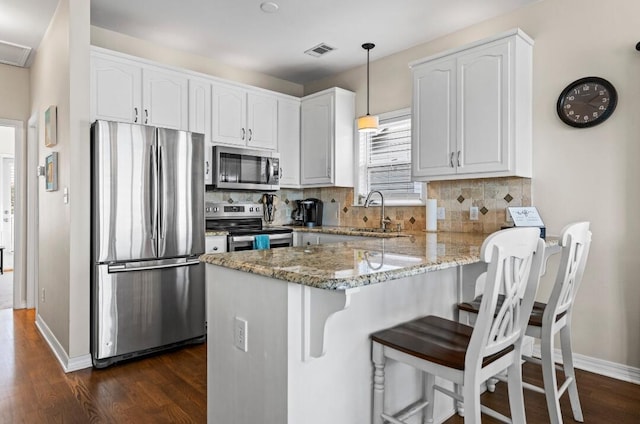 kitchen with a sink, stainless steel appliances, light stone countertops, dark wood finished floors, and a peninsula